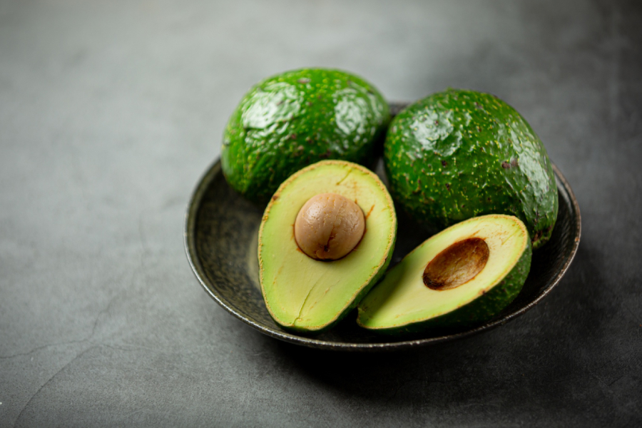 A perfectly ripe avocado half with its large pit, alongside sliced avocado pieces on a white plate.